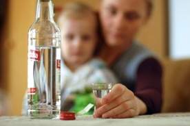 zdjęcie poglądowe - matka z dzieckiem, na stole butelka wódki i kieliszek