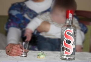 zdjęcie poglądowe - matka z dzieckiem, przed nimi na stole kieliszek i butelka wódki