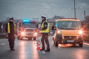 zdjęcie policjantów drogówki pracujących w miejscu wypadku, w tle pomoc drogowa i straż pożarna