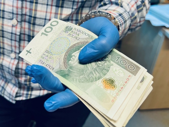 zdjęcie przedstawia plik banknotów 100 złotowych trzymanych w ręku