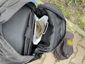 zdjęcie przedstawia otwarty plecak sprawcy z papierową torebką wypełnioną pieniędzmi