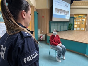 zdjęcie - policjantka z wydziału doboru, a w tle siedząca na krześle uczennica z goglami do wirtualnej rzeczywistości może wcielić się w policjantkę biorącą udział w akcji