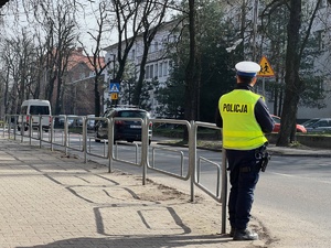 zdjęcie z policyjnych działań - policjant z drogówki stojący przy drodze obserwuje przejście dla pieszych przy szkole podstawowej